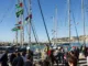 Sous un ciel bleu, une cinquantaine de personnes sont à quai devant une dizaine de voiliers dont les mâts et gréements sont ornés de drapeaux et fanions aux couleurs palestiniennes.